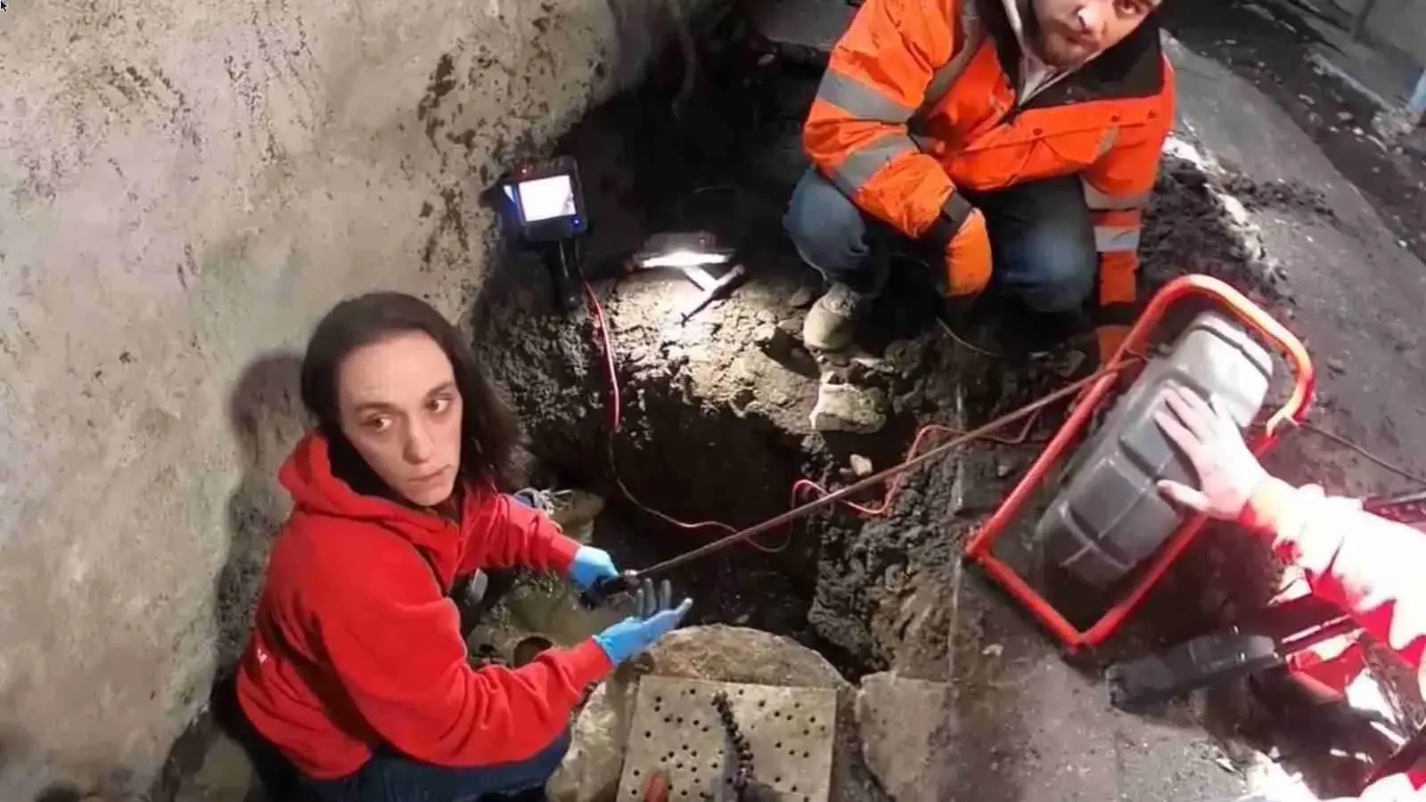 Emergency crew running a sewer camera inspection in a dug pit
