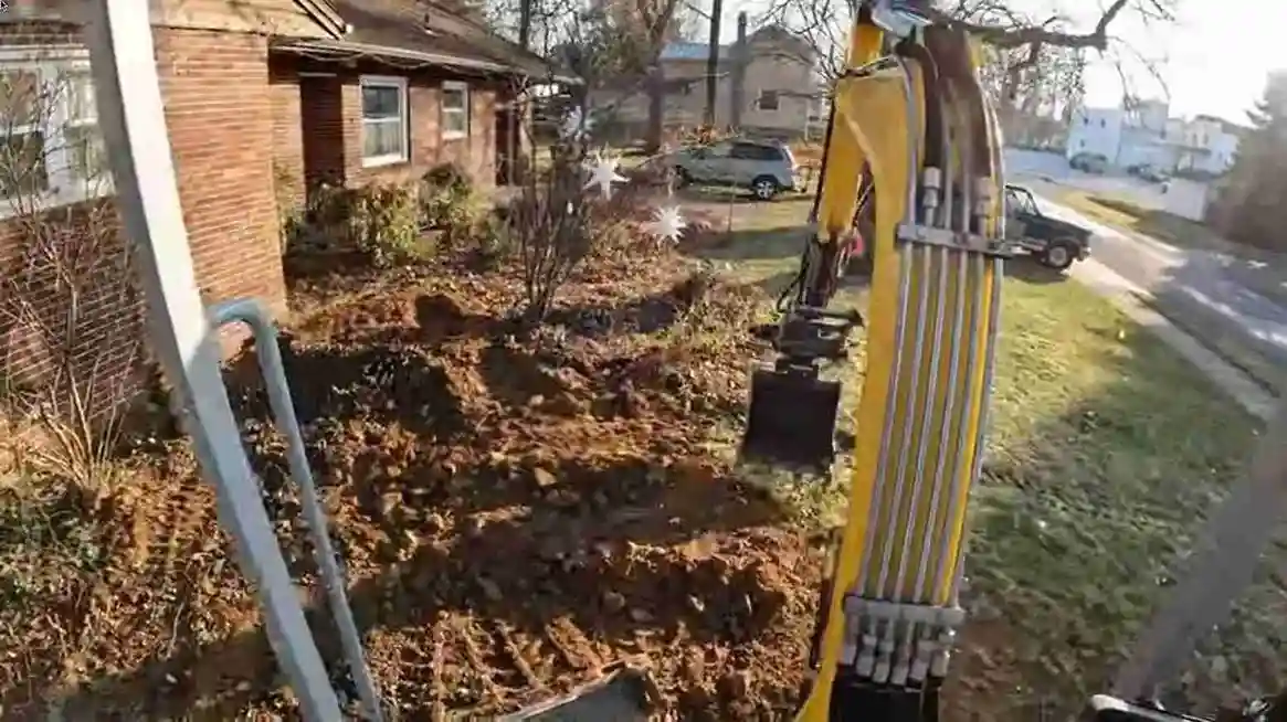 Excavator backfilling a sewer trench in a front yard