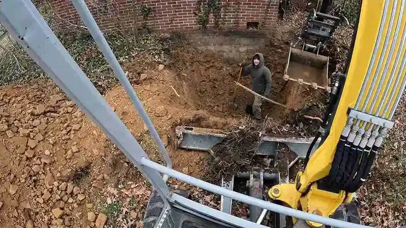 Excavator arm over a deep sewer dig at a brick house
